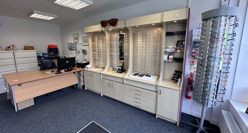 An optician's office with a desk, computer, cabinets displaying eyeglasses, and a rotating rack of glasses.